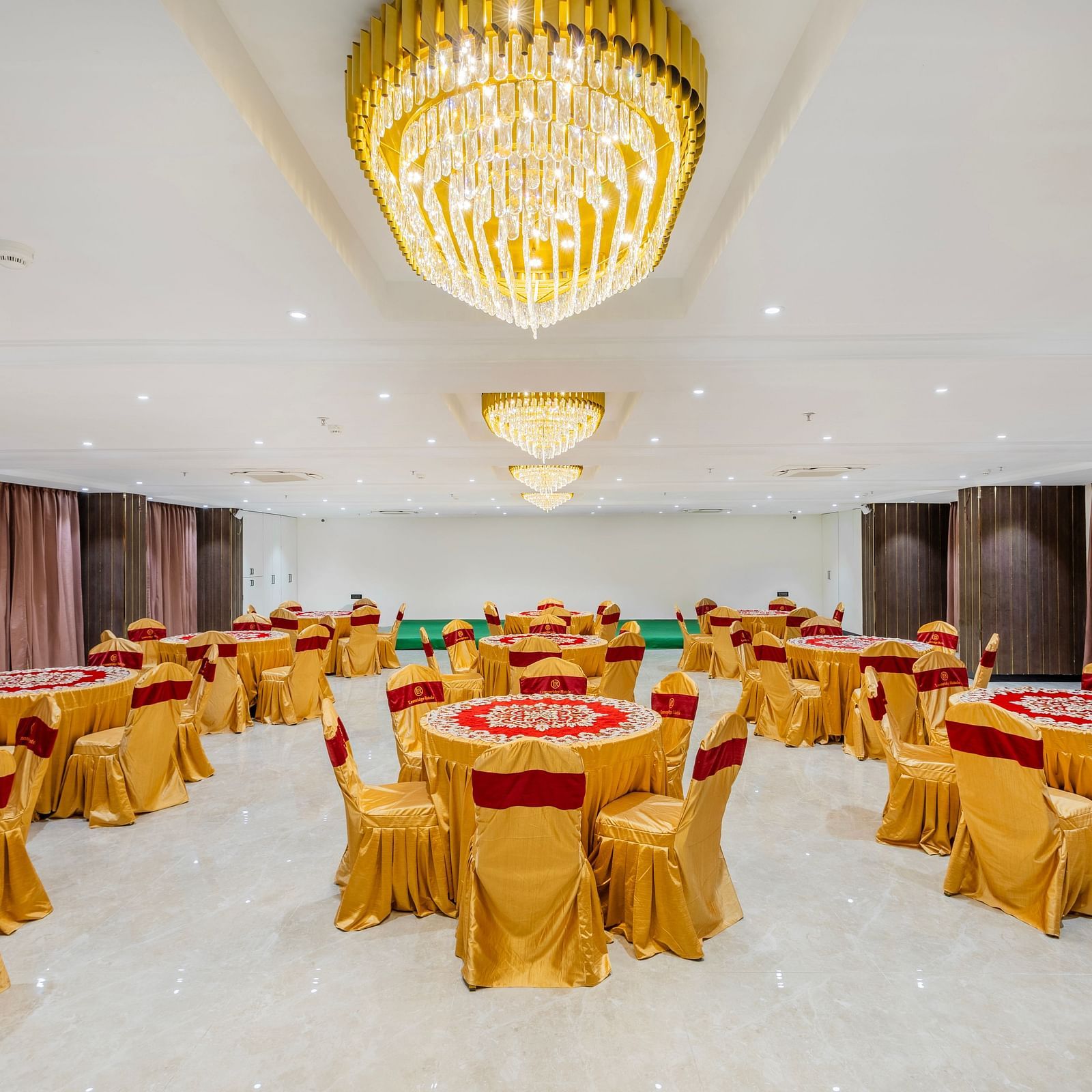 Lemonridge Hotels, KPHB | Banquet hall with round dining tables and chairs, featuring a unique ceiling light.